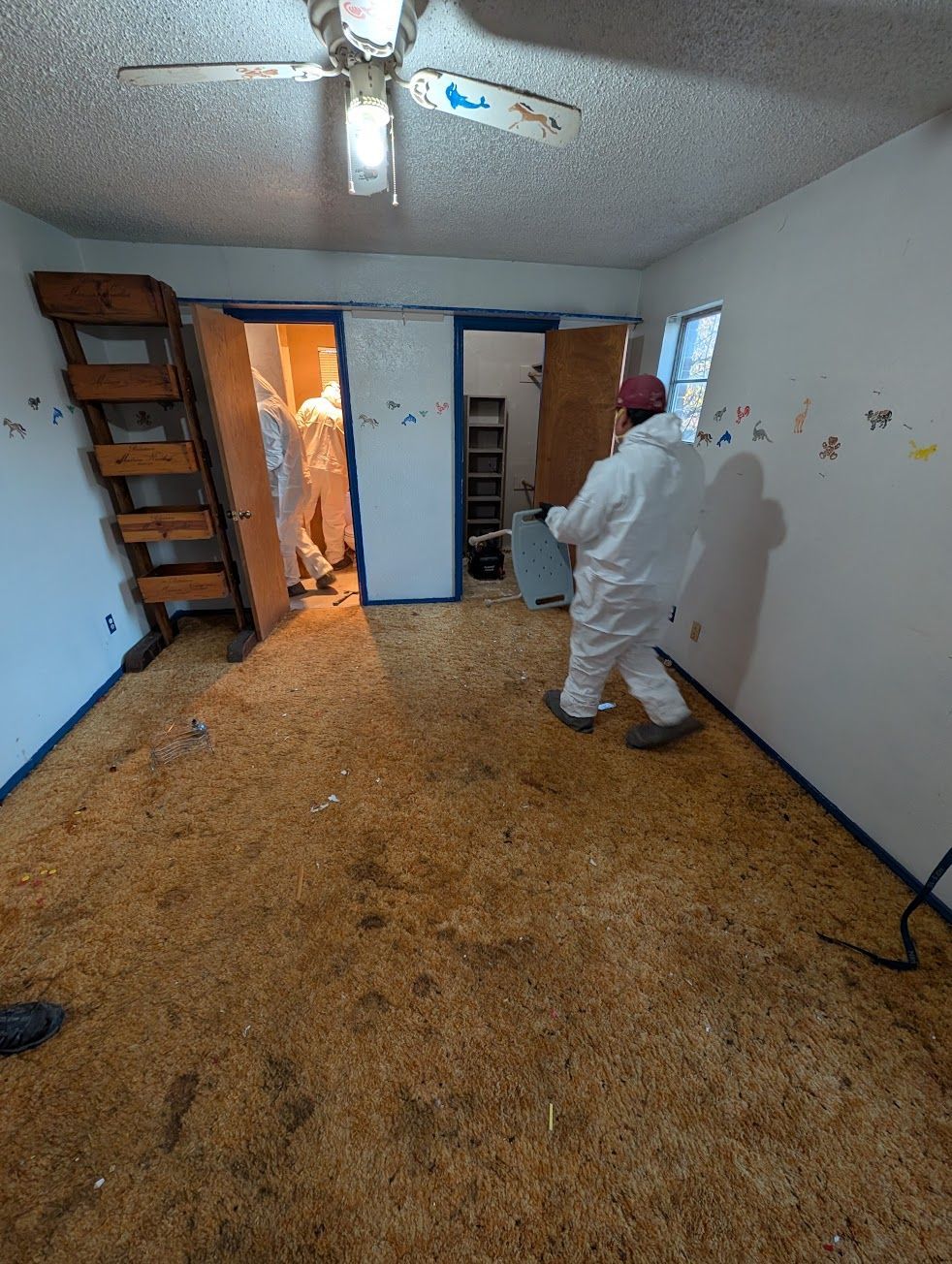 A person in a protective suit is cleaning a microwave in a kitchen.