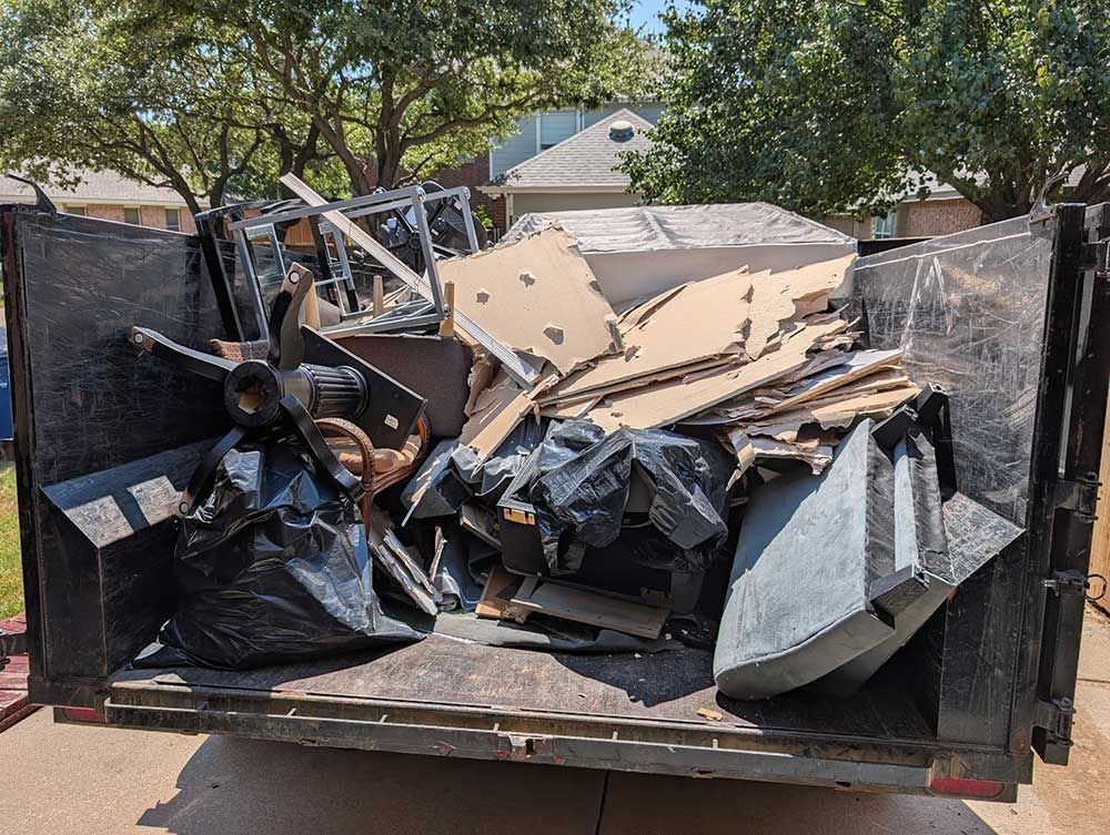 Dumpster filled with debris, including wood, cardboard, and black trash bags, outdoors.