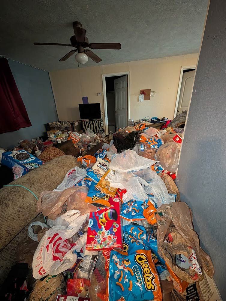 Room filled with piles of trash and bags, including snack bags, rug, and TV in the background.