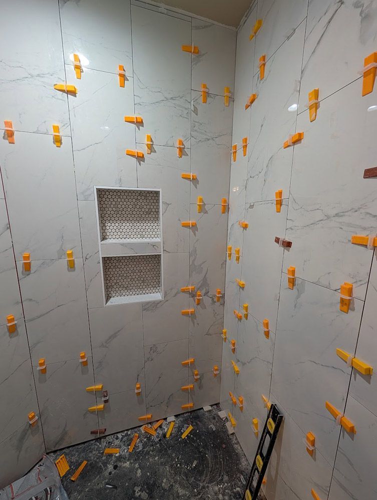 Bathroom walls tiled with large, white marble-look tiles, orange tile leveling spacers used.