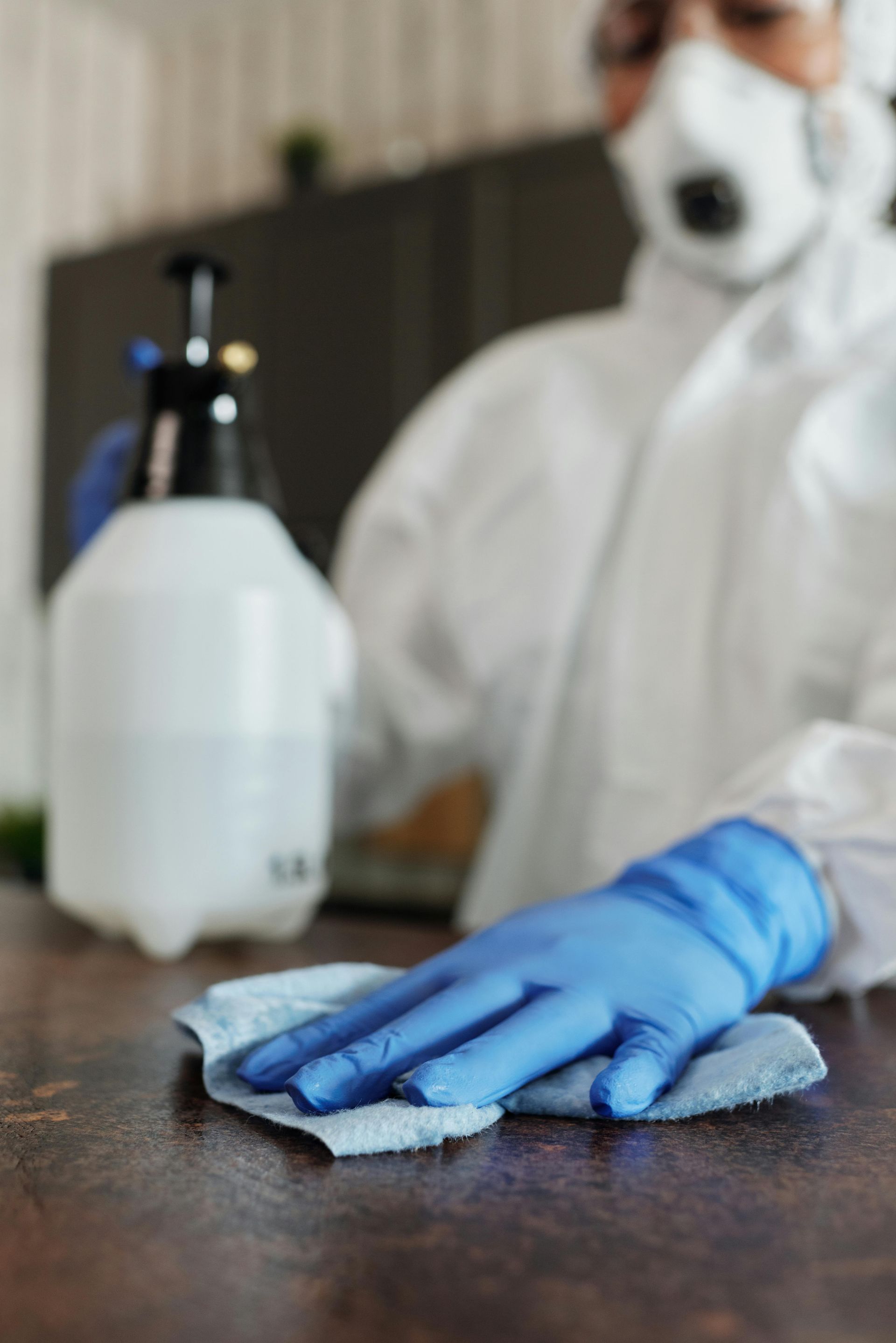 A person in a protective suit is cleaning a table with a cloth.