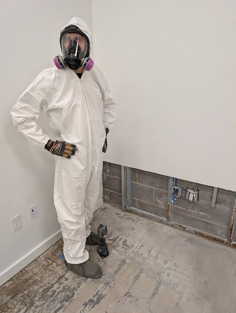 Person in protective suit and respirator stands in a room with water damage.