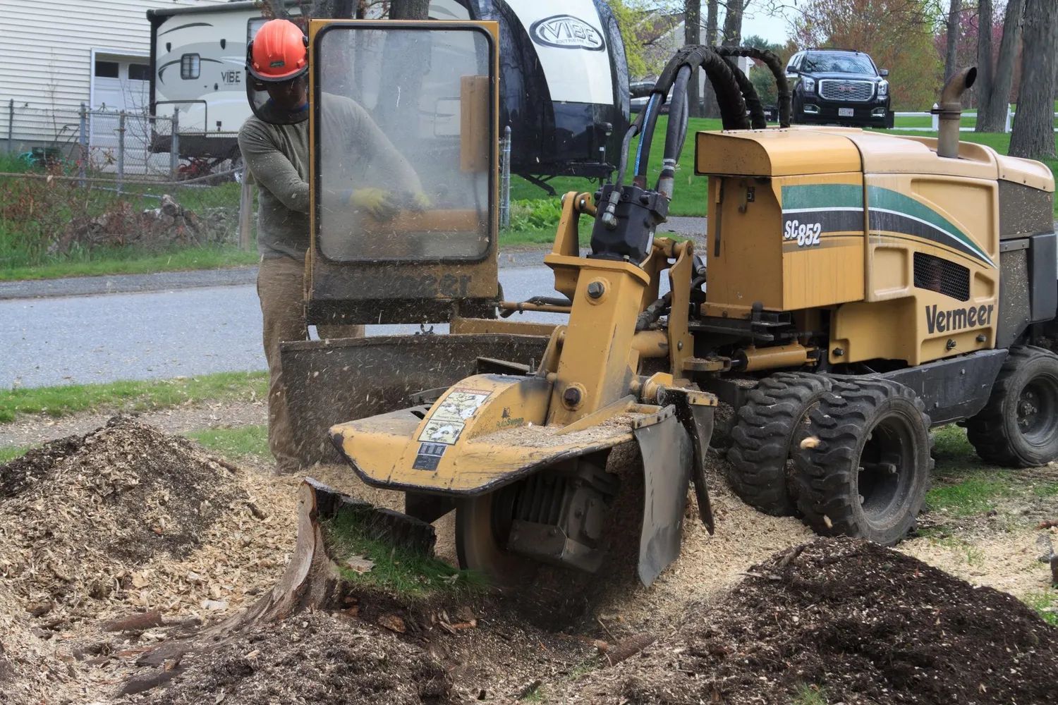 A worker operates a yellow stump grinder, removing a tree stump.