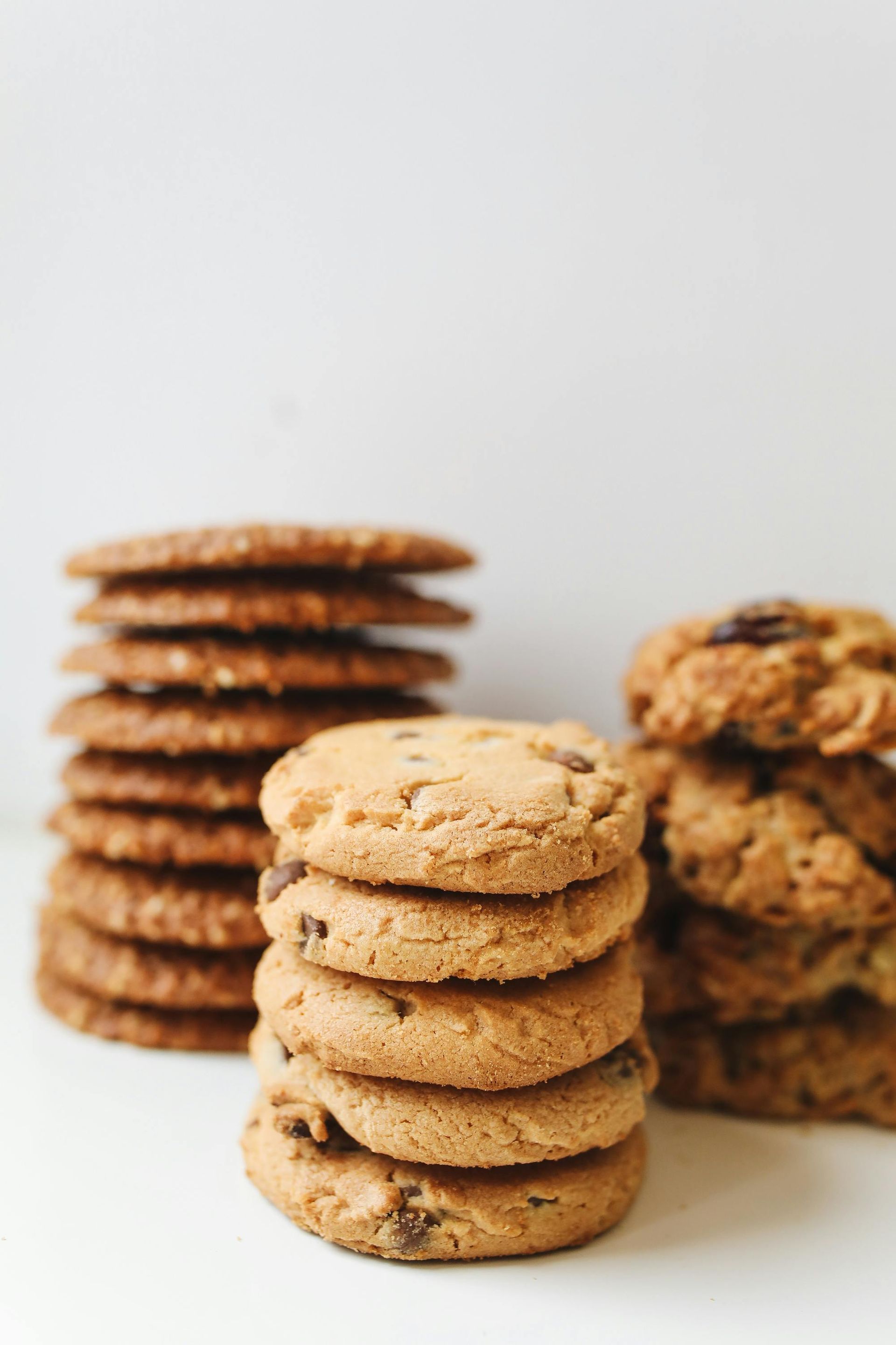 Stacks of chocolate chip, peanut butter, and other cookies on a white surface.