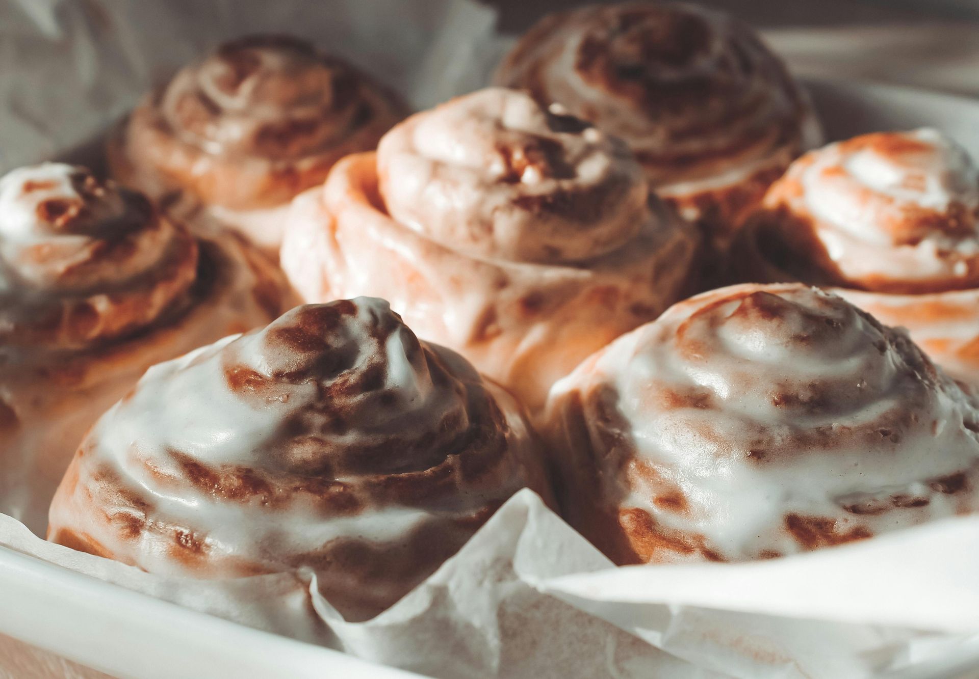 Cinnamon rolls with white icing in a white rectangular container.