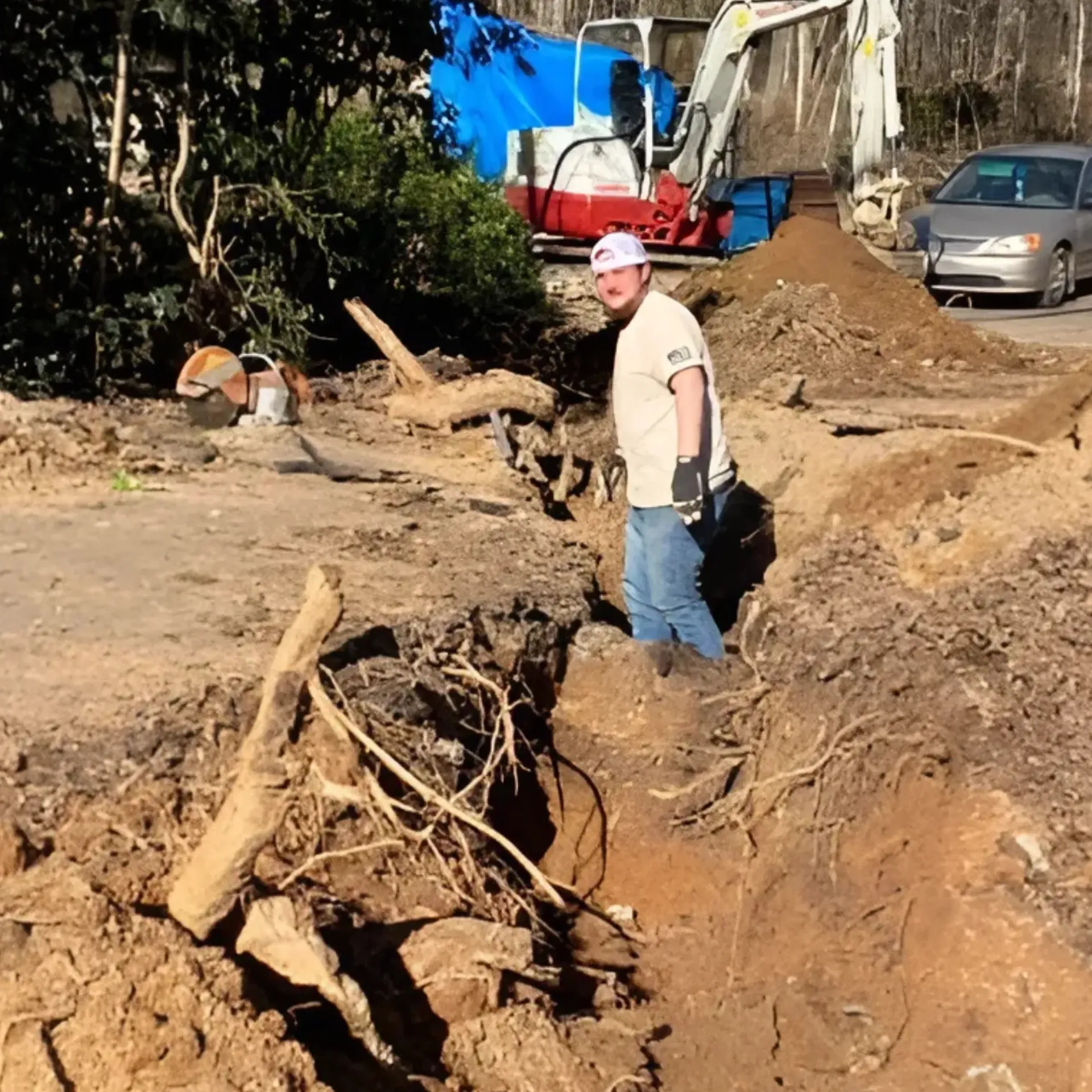 Brothers Landscaping - A man is standing in a pile of dirt in front of an excavator