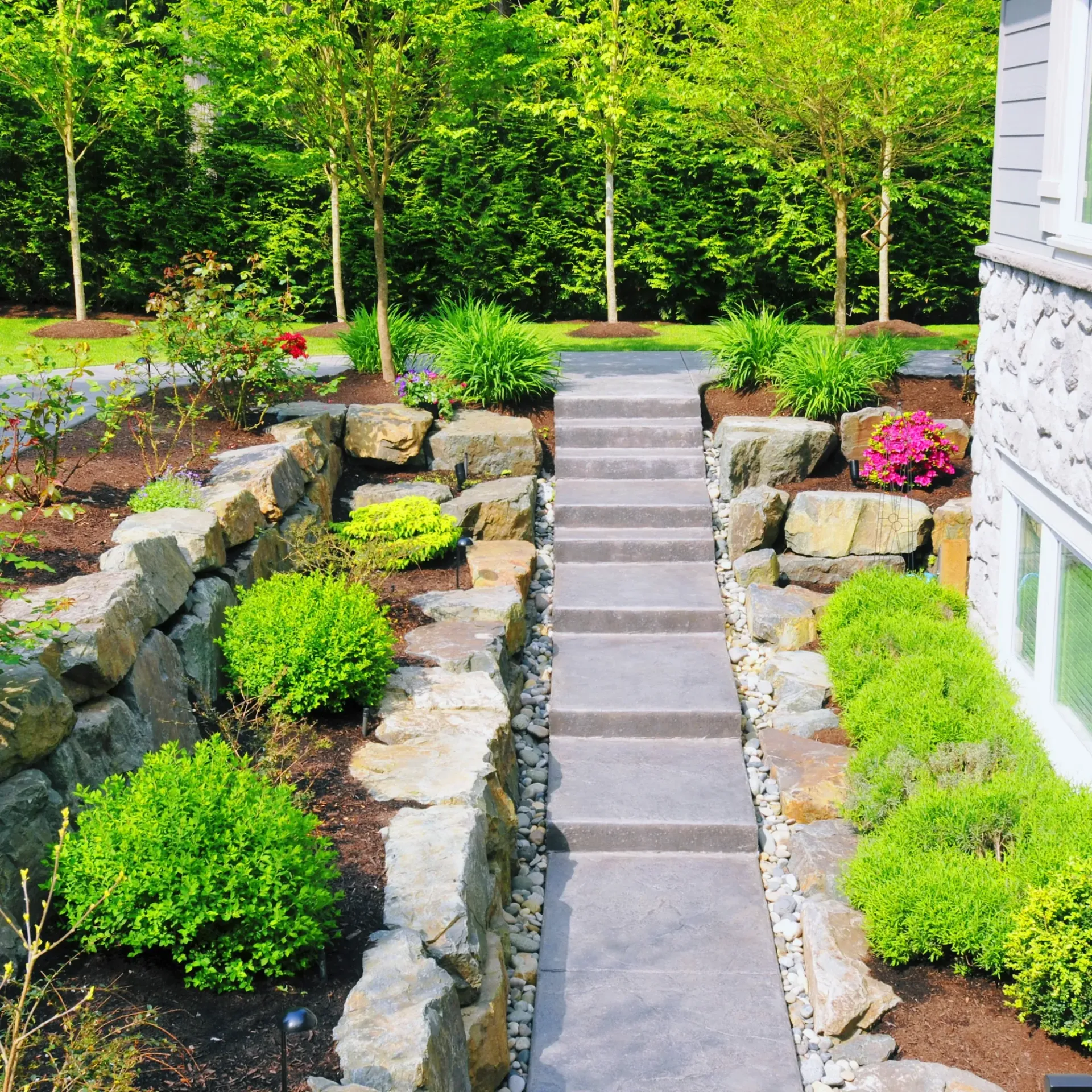 Brothers Landscaping - A stone walkway leading to a house surrounded by trees and bushes