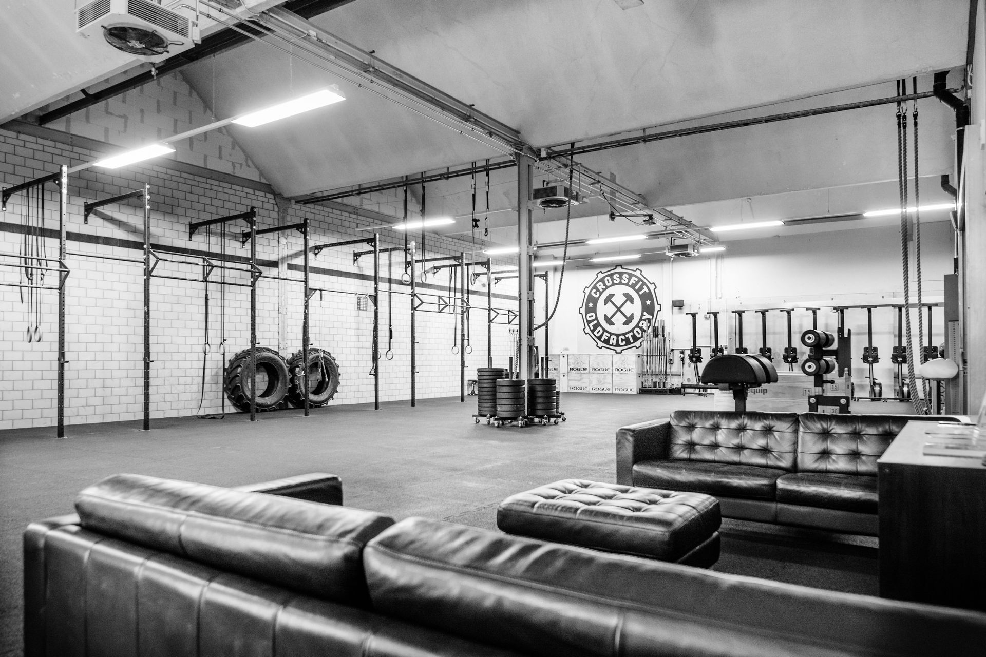 Fitnessstudio-Interieur mit Klimmzugstangen, Gewichten und Sitzbereich mit Ledersofa.