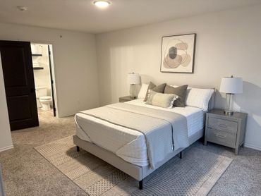 A bedroom with a large bed , nightstands , lamps and a painting on the wall.