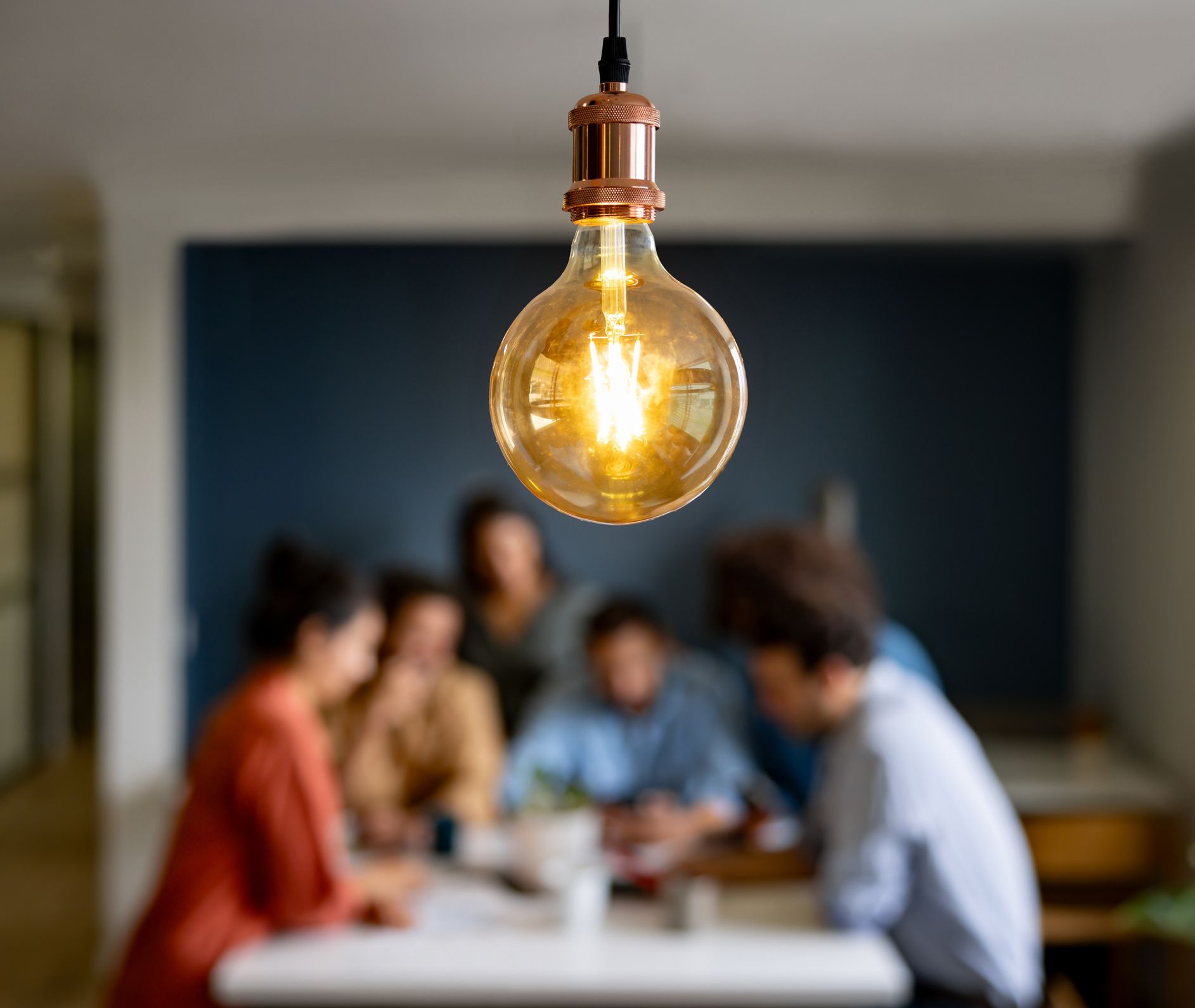 A group of people are sitting around a table with a light bulb hanging from the ceiling.