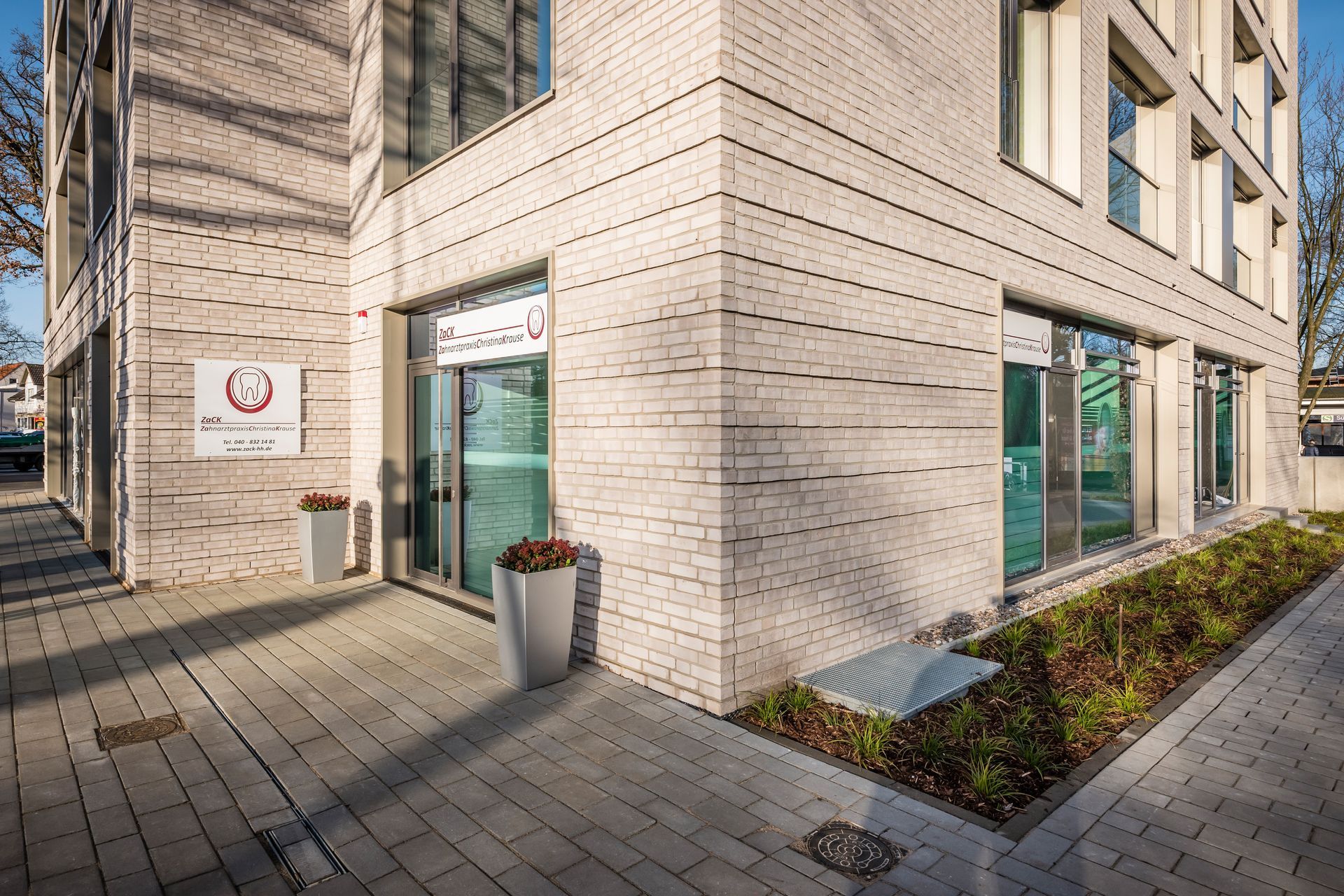 Ein großes weißes Backsteingebäude mit vielen Fenstern und Pflanzkübeln davor.