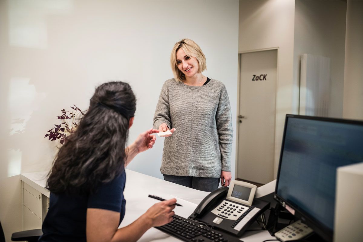 Eine Frau gibt einer anderen Frau an einem Schreibtisch eine Karte.