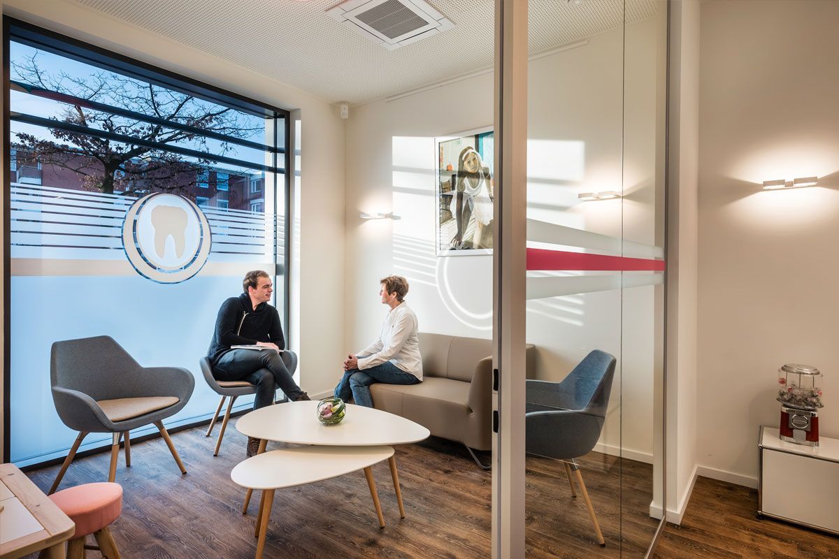 Zwei Männer sitzen auf einer Couch in einem Wartezimmer.