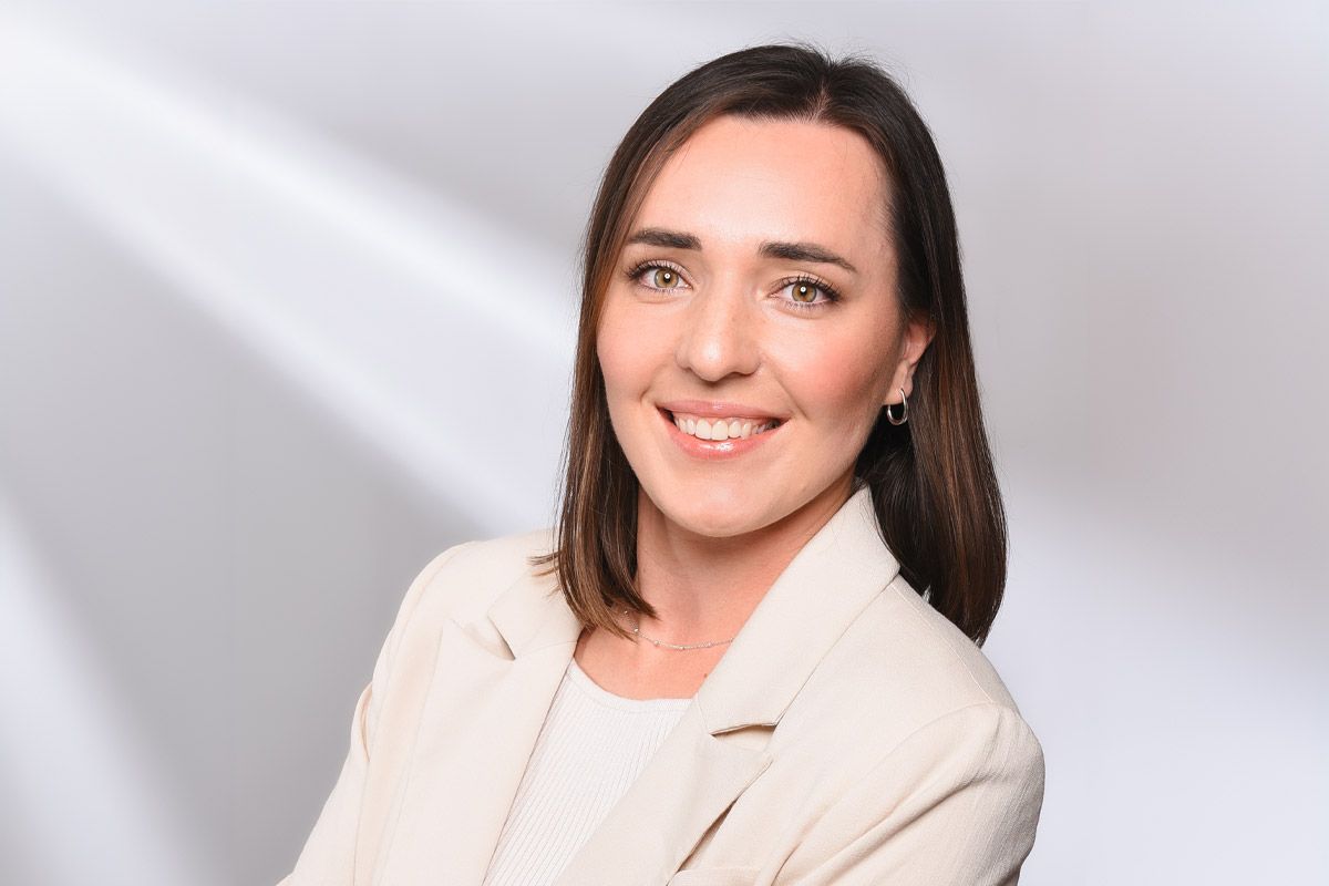 Eine Frau in einer weißen Jacke lächelt in die Kamera.