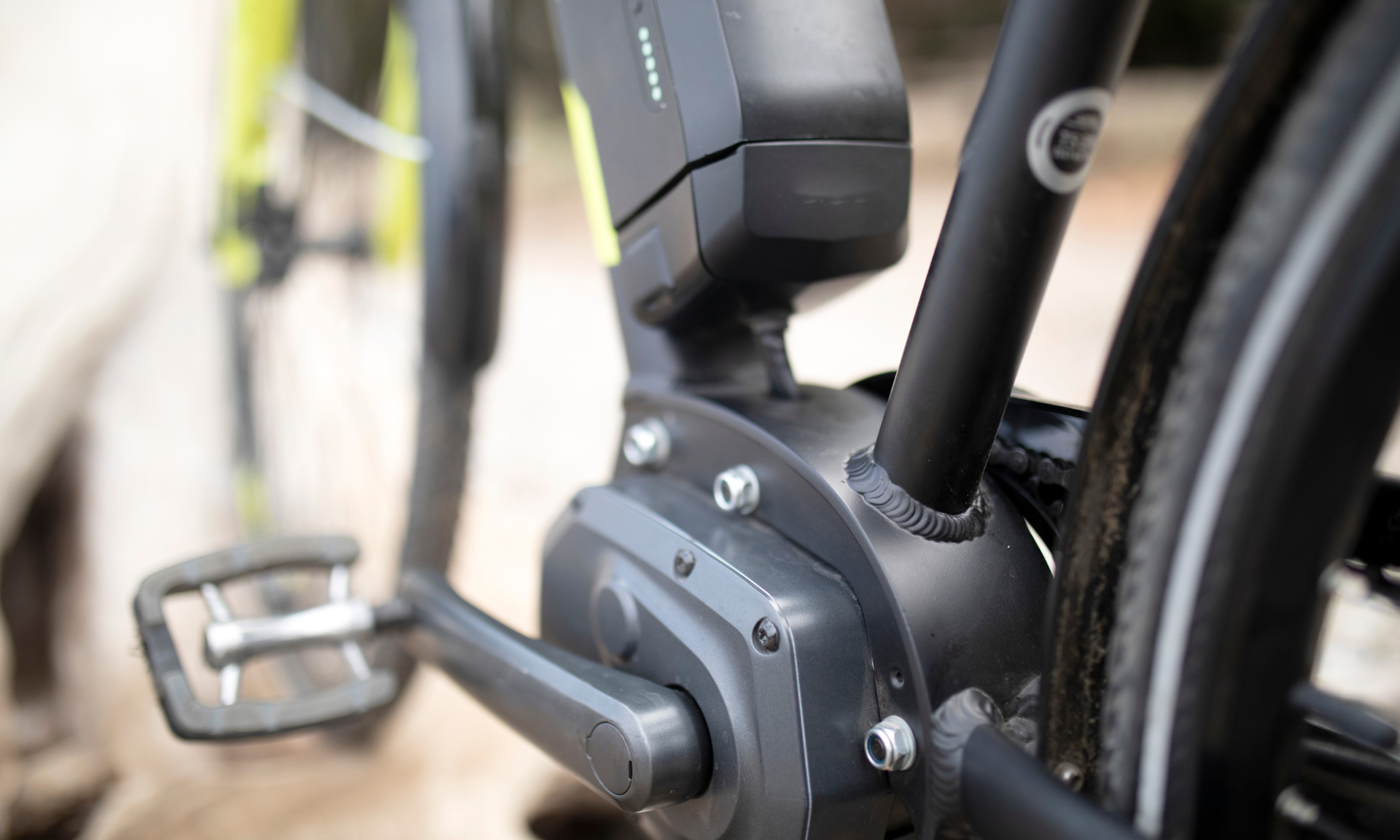 Close-up van de motor en accu van een zwarte elektrische fiets tegen een wazige buitenachtergrond.