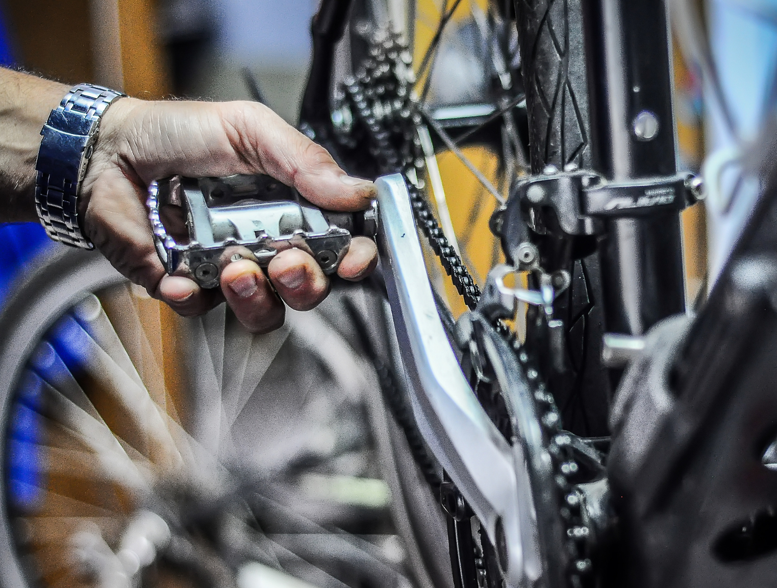 Hand houdt fietspedaal vast tijdens reparatie; ketting en fietswiel zichtbaar.
