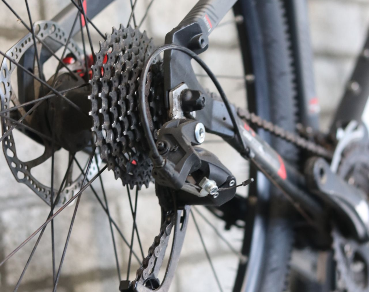 Close-up van het achterwiel van een fiets, met cassette, derailleur en schijfrem.