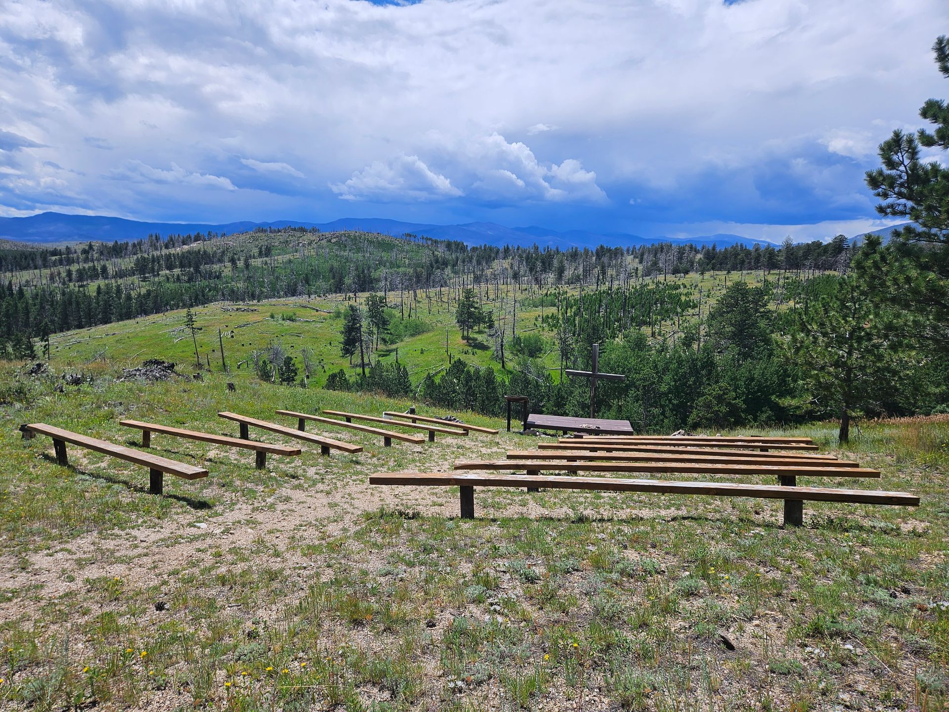 Benches on hillside overlooking view of clouds and mountains.