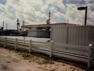 Shell gas station behind a white picket fence under a cloudy sky