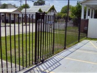 Black metal fence bordering a sidewalk and grassy area in front of houses