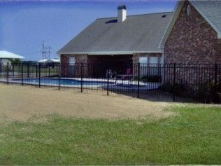 A brick house with a pool enclosed by a black metal fence