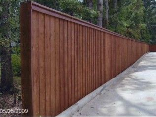 Brown wooden privacy fence along a curved concrete surface with trees in the background