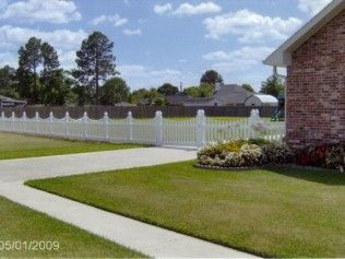 A white picket fence surrounds a green lawn and concrete driveway