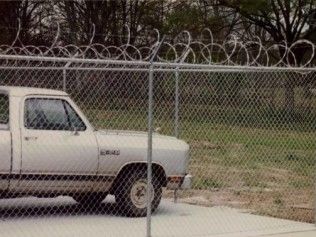 White pickup truck behind chain-link fence topped with razor wire