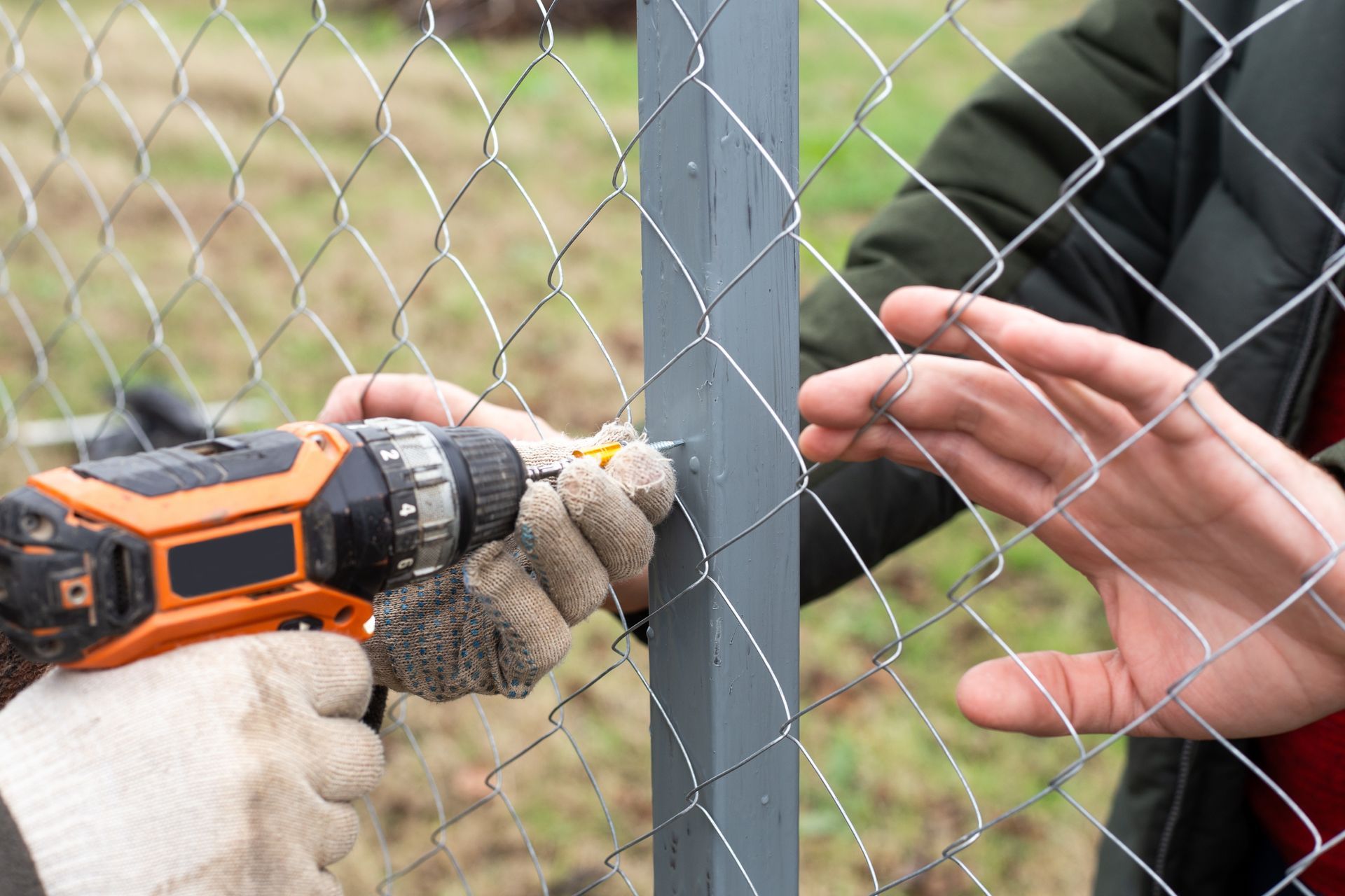 Person using a drill to attach chain-link fence to a gray post