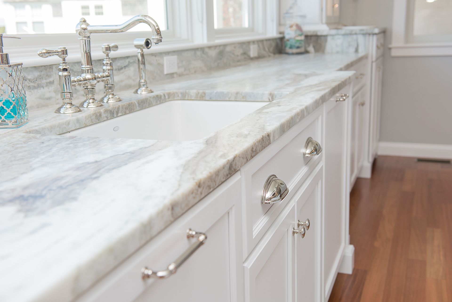 Bright white bathroom vanity with marble countertop, chrome faucet, and warm wood floor.