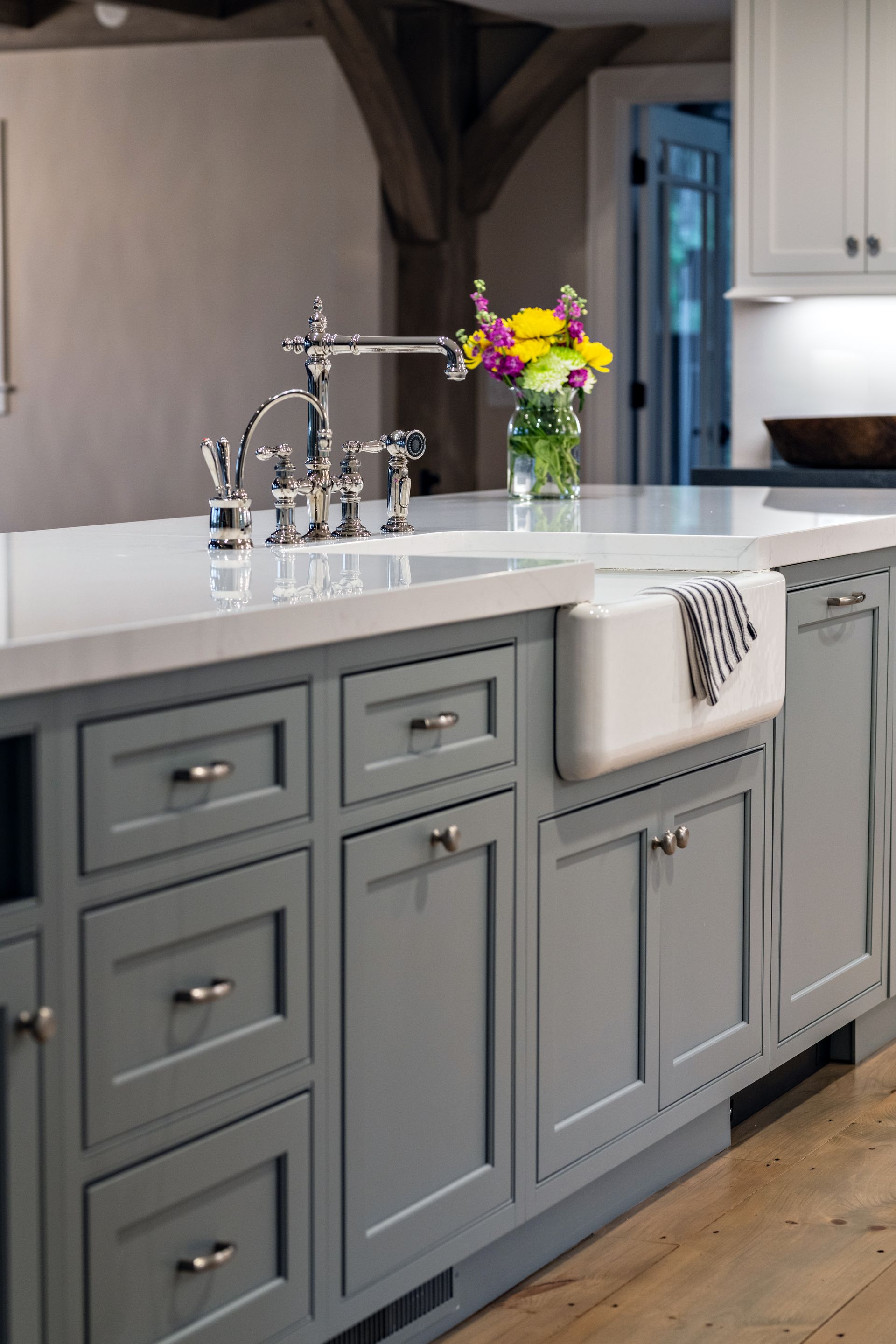 Gray kitchen island with white countertop, chrome faucet, and a vase of colorful flowers