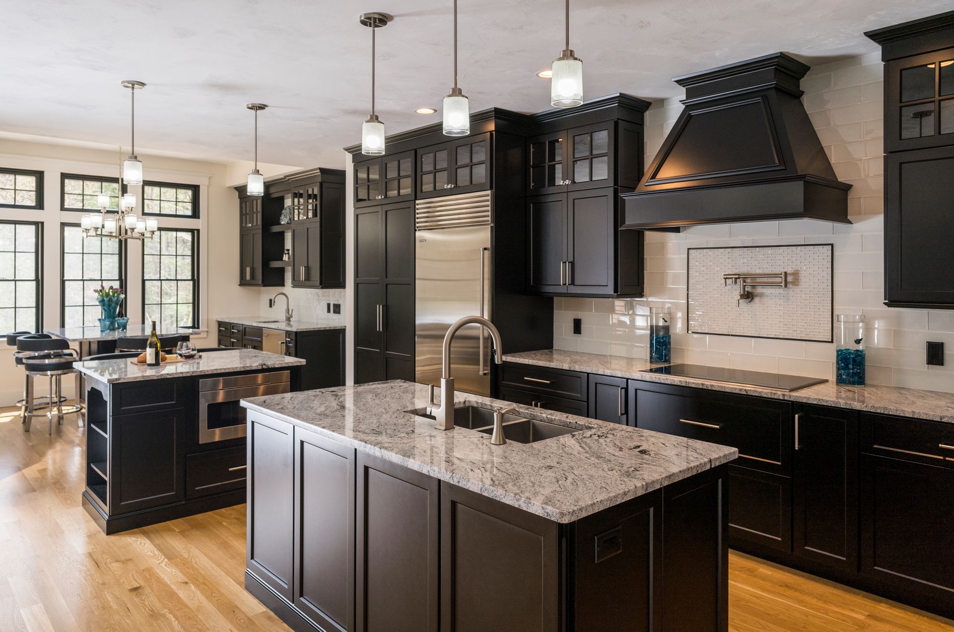 Modern kitchen with dark cabinets, granite island, pendant lights, and stainless steel appliances