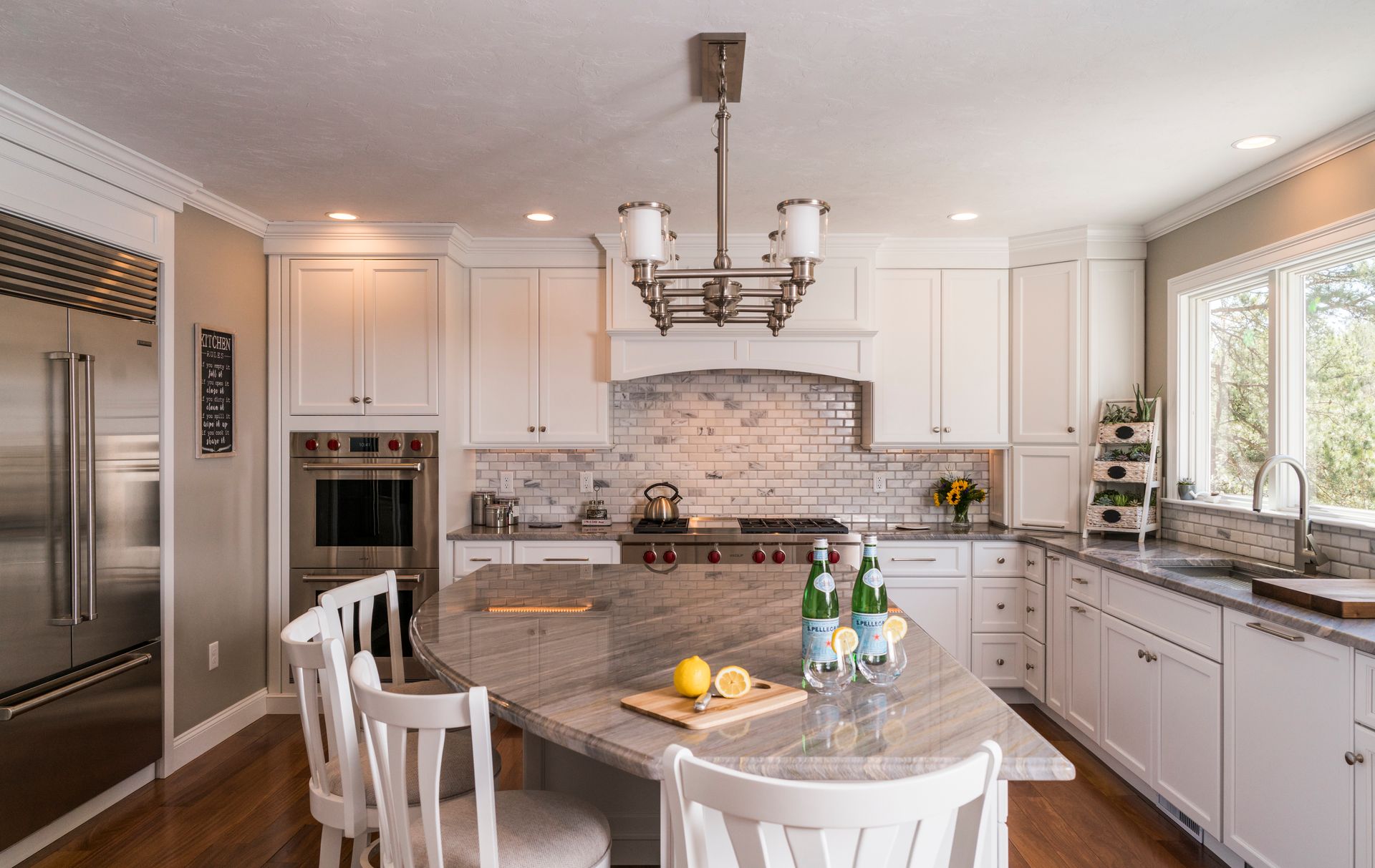 Bright kitchen with white cabinets, granite island, chandelier, and stainless steel appliances.