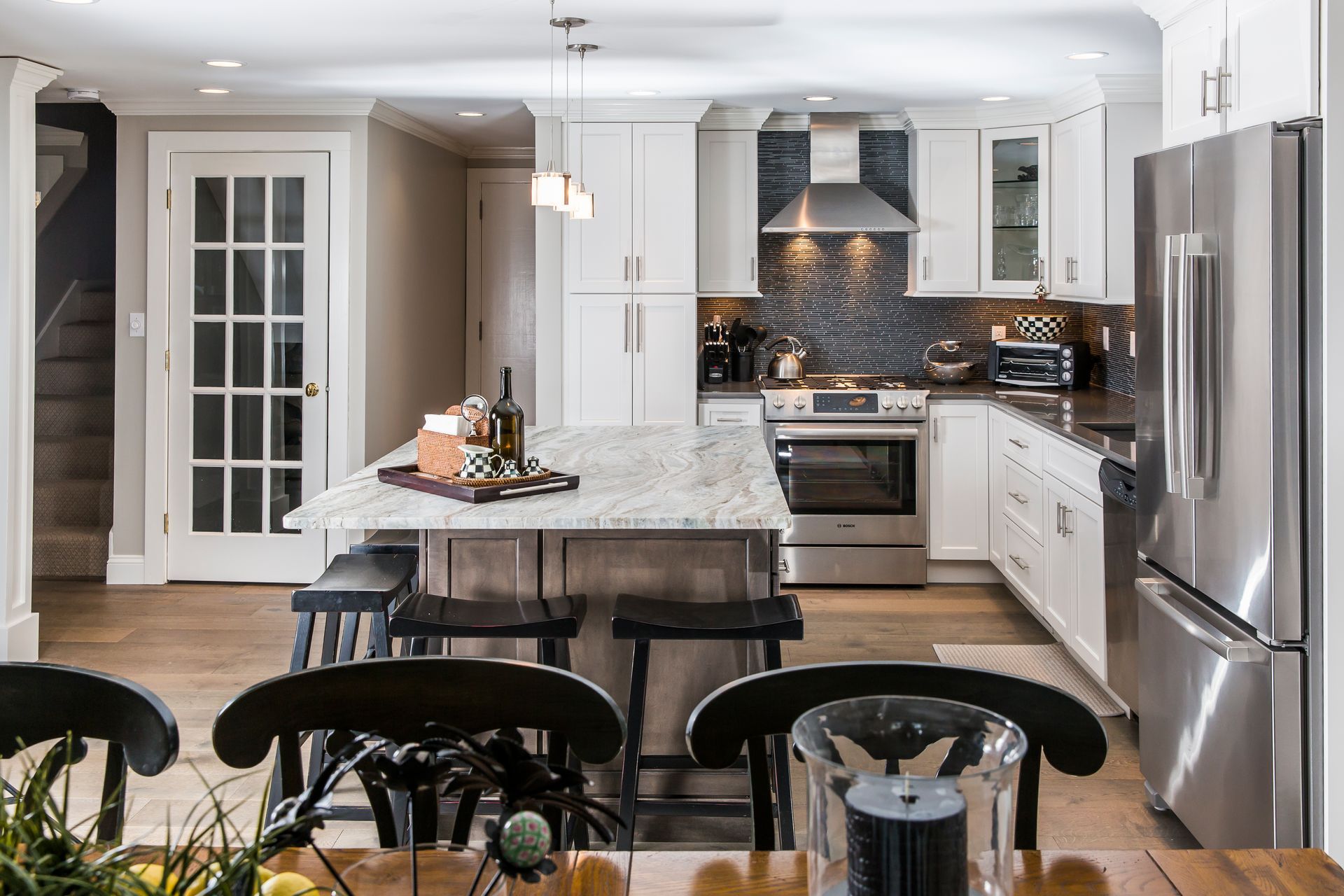 Bright modern kitchen with white cabinets, stainless appliances, island, and black bar stools