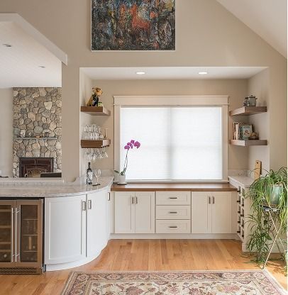 Bright living room nook with built-in shelves, white cabinets, wood floor, and a large window with orchid and plants