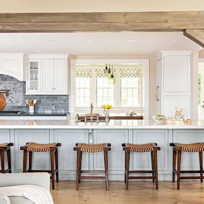 Bright white kitchen with blue island, bar stools, and a windowed dining nook under exposed wood beams