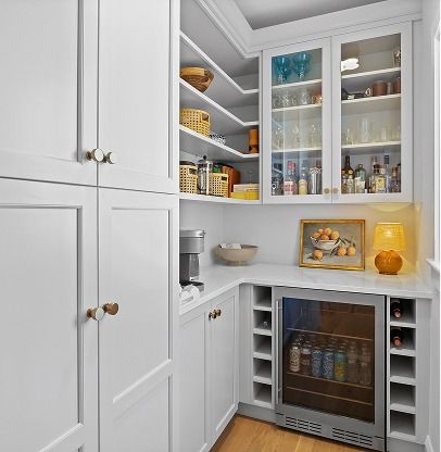 White kitchen pantry with open shelves, glass-door cabinet, wine fridge, and neatly organized snacks and bottles