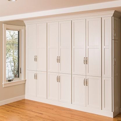 Built-in white bedroom cabinets with silver handles beside a window and hardwood floor