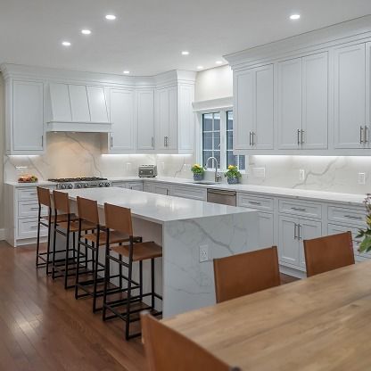 Bright modern white kitchen with marble island, bar stools, and hardwood floor