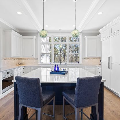 Bright modern kitchen with white cabinets, large island, blue chairs, and pendant lights