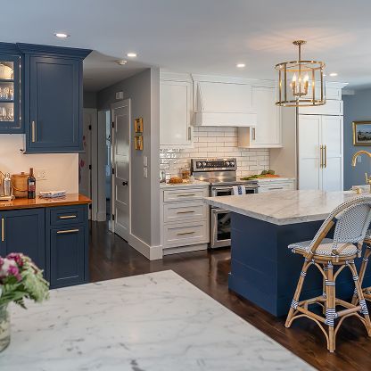 Bright kitchen with navy and white cabinets, marble island, wicker stools, and brass pendant light