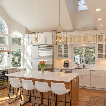 Bright modern kitchen with white cabinets, large island, pendant lights, and tall windows.