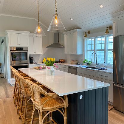 Bright modern kitchen with white cabinets, large island, wicker stools, and pendant lights
