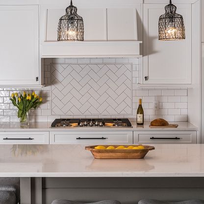Bright white kitchen with herringbone tile backsplash, pendant lights, flowers, and a bowl of lemons on the island