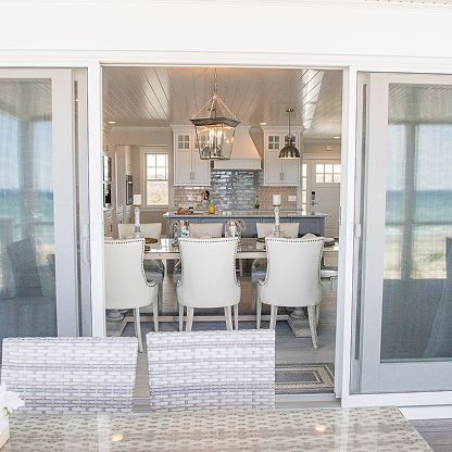 Bright seaside patio with sliding doors open to a white dining room and ocean view