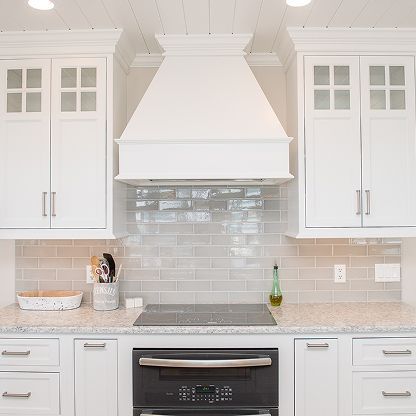 Bright white kitchen with shaker cabinets, subway tile backsplash, gray counters, and a stainless oven under a hood.