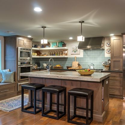 Modern kitchen with gray island, three stools, light blue backsplash, and stainless steel appliances