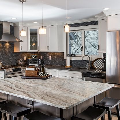 Modern kitchen with large marble island, stainless steel appliances, white cabinets, and pendant lights