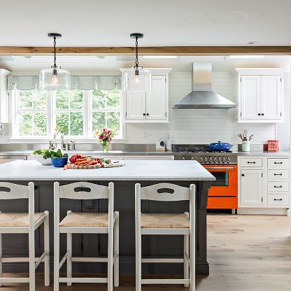 Bright modern kitchen with white cabinets, a large island, pendant lights, and an orange stove.