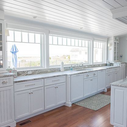 Bright white kitchen with large windows, marble countertops, and light wood floors